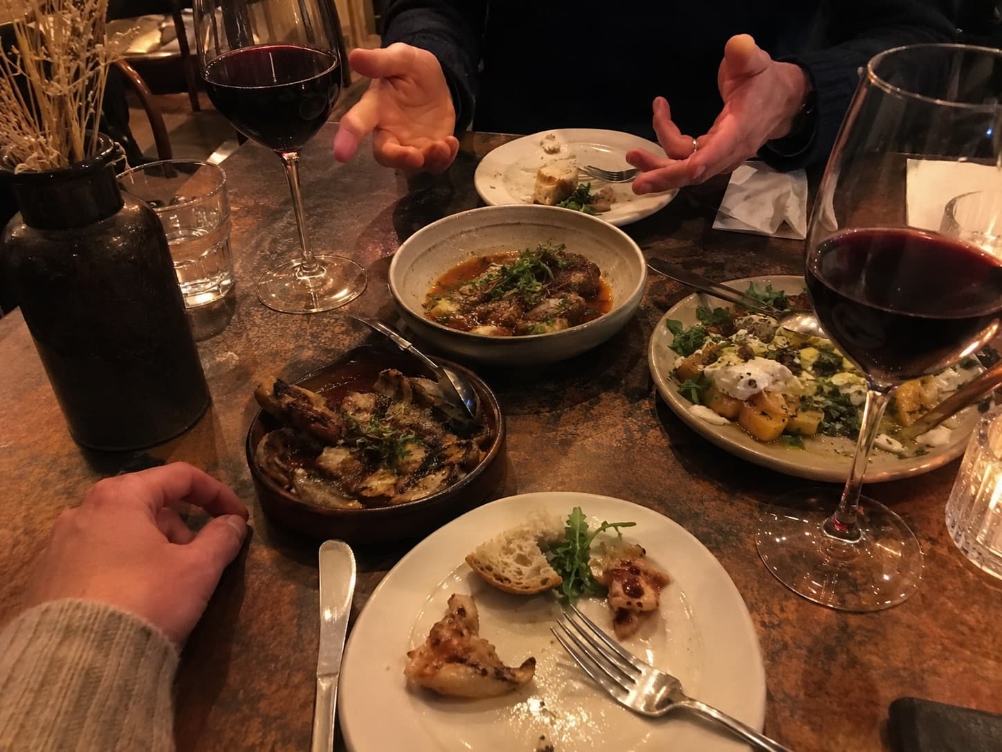 Two people talking over a shared dinner, wine and small plates between them